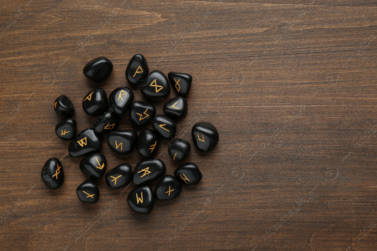 Photo of Pile of black rune stones on wooden table, flat lay. Space for text