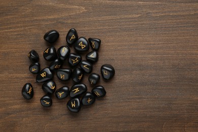 Photo of Pile of black rune stones on wooden table, flat lay. Space for text