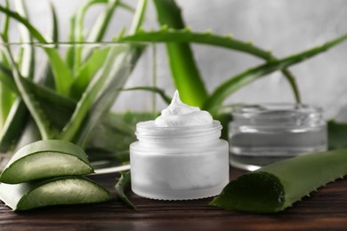 Jar of cosmetic product and cut aloe vera leaves on wooden table, closeup