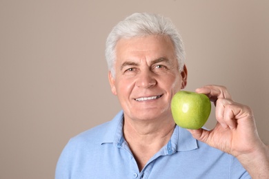 Photo of Mature man with healthy teeth and apple on color background