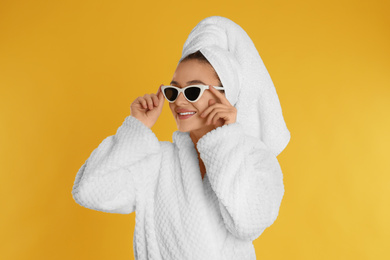 Photo of Beautiful young woman in bathrobe and sunglasses on yellow background