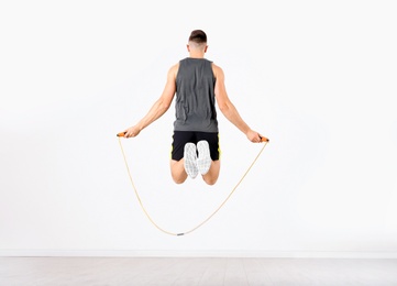 Photo of Sportive man training with jump rope in light room