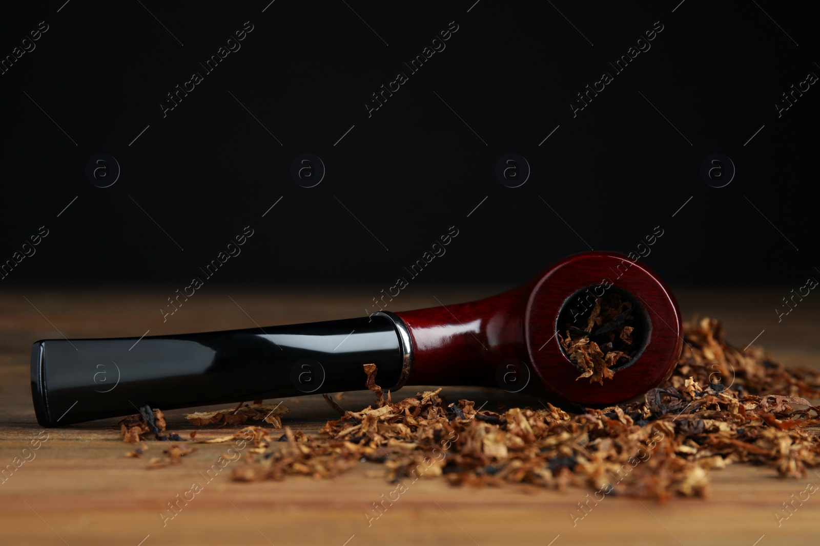 Photo of Smoking pipe and dry tobacco on wooden table against dark background. Space for text