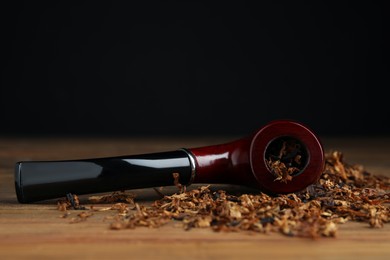 Photo of Smoking pipe and dry tobacco on wooden table against dark background. Space for text