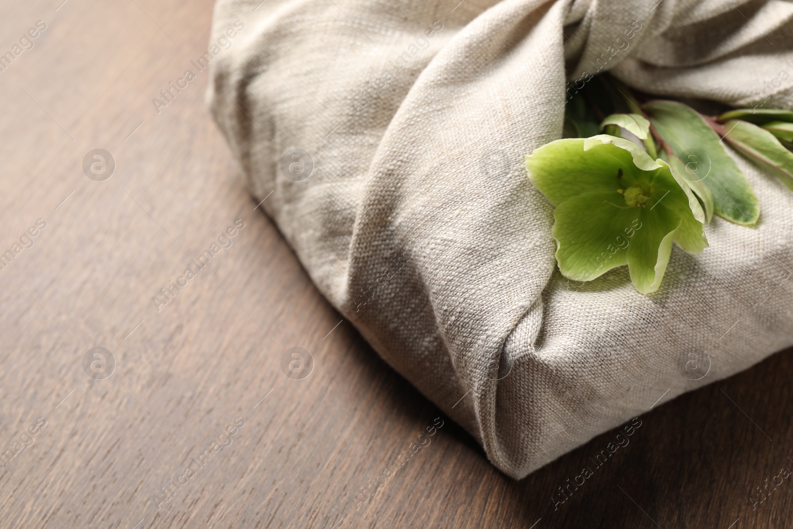 Photo of Furoshiki technique. Gift packed in white fabric decorated with beautiful flowers on wooden table, closeup. Space for text