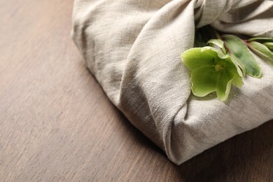 Photo of Furoshiki technique. Gift packed in white fabric decorated with beautiful flowers on wooden table, closeup. Space for text