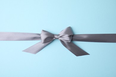 Photo of Grey satin ribbon with bow on light blue background, top view