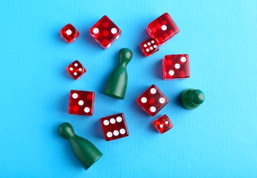 Photo of Many red dices and color game pieces on light blue background, flat lay