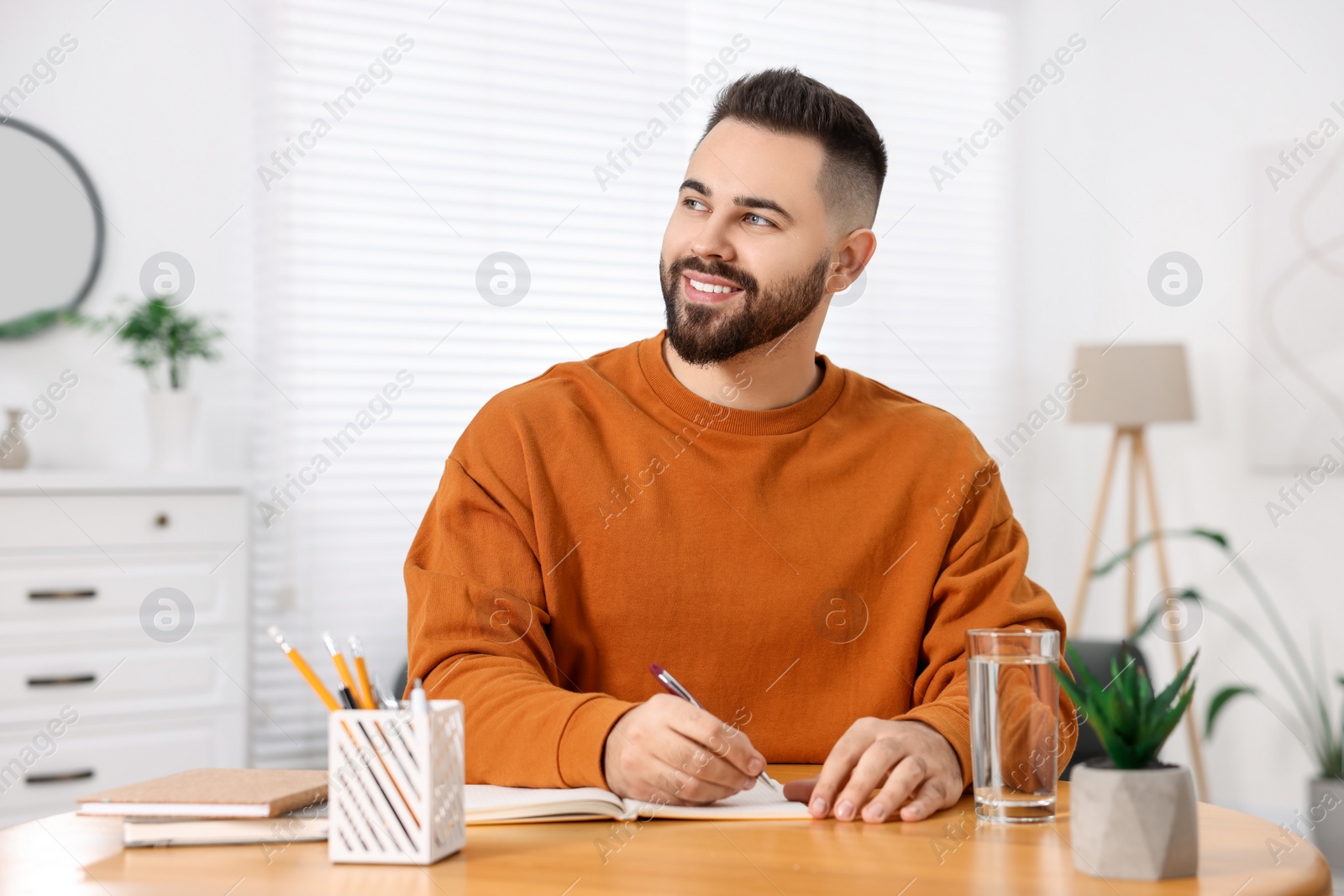 Photo of Young man writing in notebook at wooden table indoors