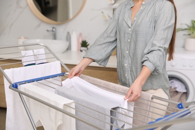 Young woman hanging clean laundry on drying rack in bathroom, closeup