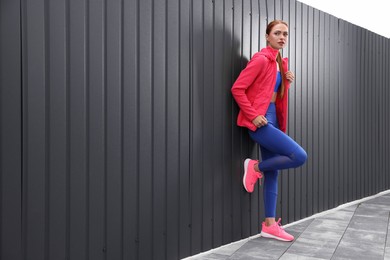 Beautiful woman in gym clothes posing near dark grey fence on street, space for text