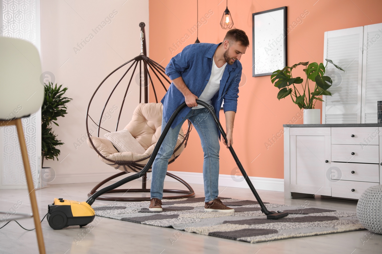 Photo of Young man using vacuum cleaner at home