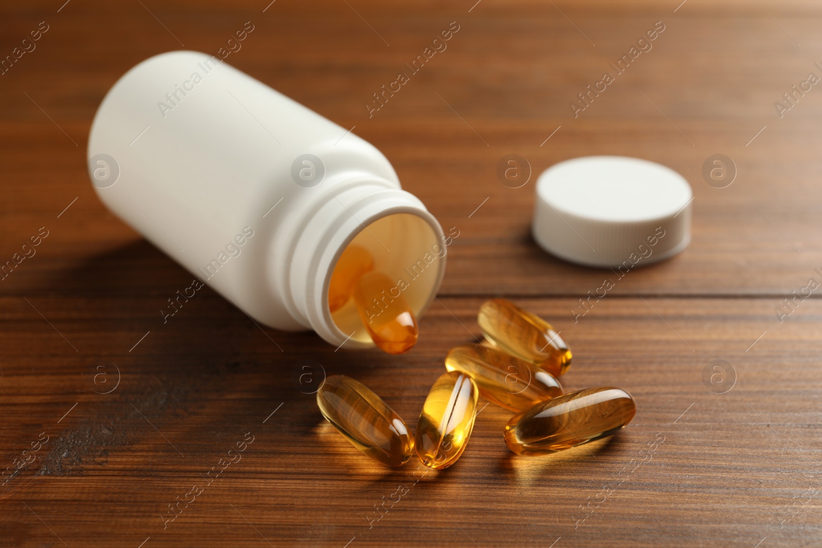 Photo of Overturned bottle with dietary supplement capsules on wooden table