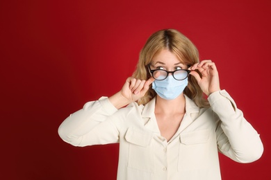 Photo of Woman wiping foggy glasses caused by wearing medical mask on red background