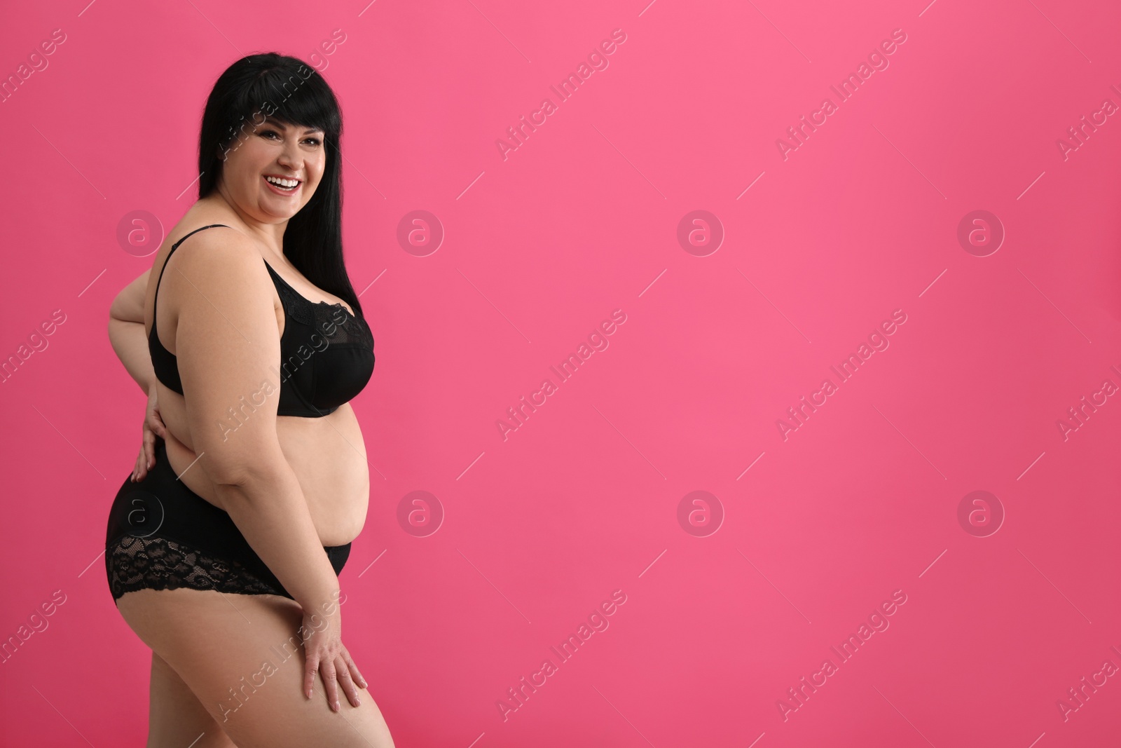 Photo of Beautiful overweight woman in black underwear on pink background, space for text. Plus-size model