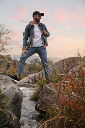 Photo of Man with backpack crossing mountain river on autumn day