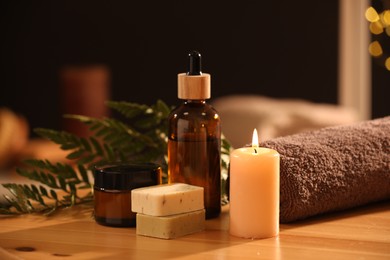 Photo of Spa composition. Cosmetic products, burning candle and towel on wooden table