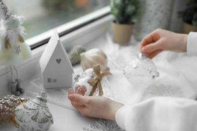 Photo of Woman holding Christmas baubles near window sill indoors, closeup
