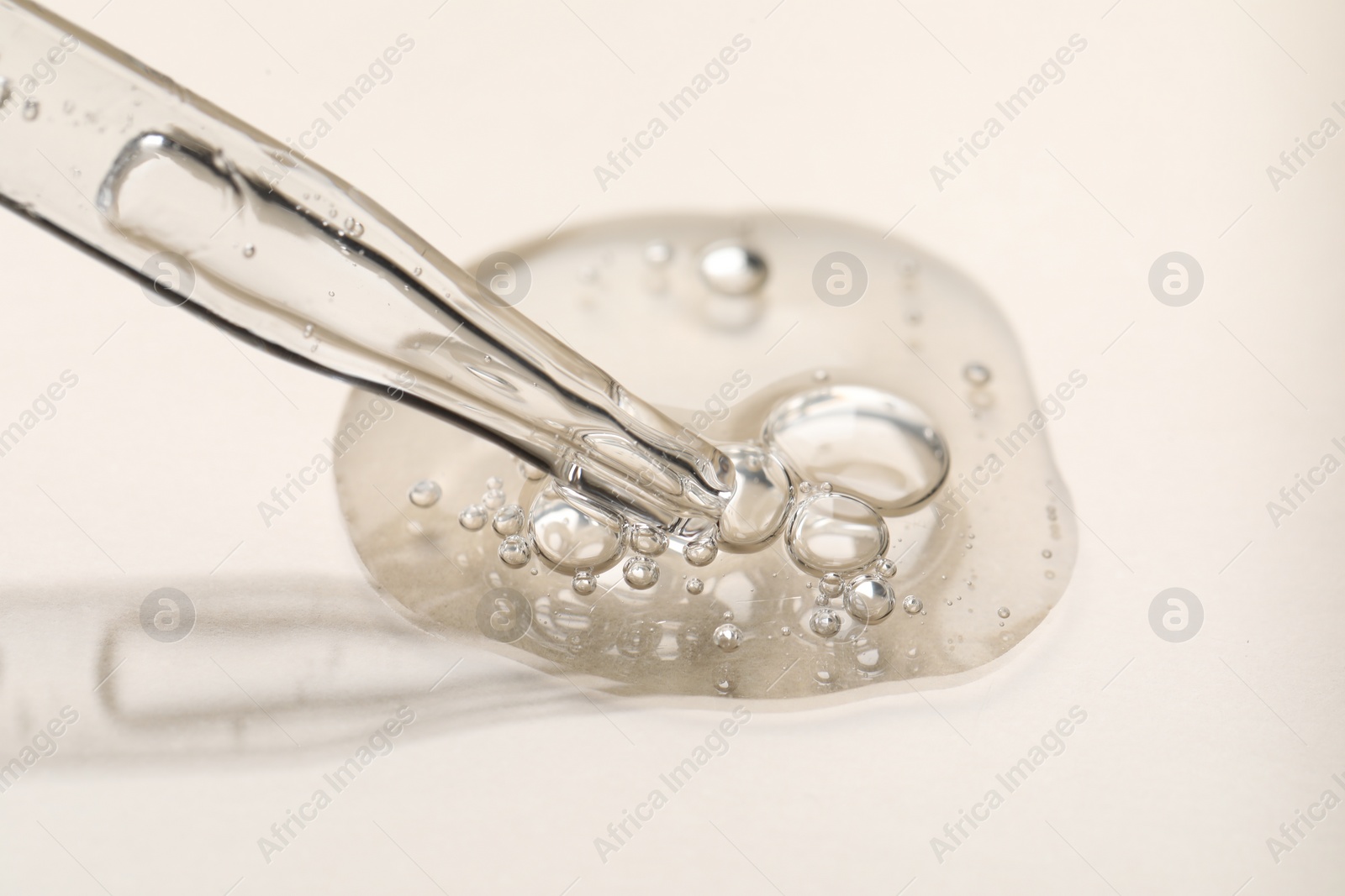 Photo of Glass pipette and transparent liquid on beige background, closeup