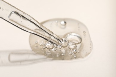 Photo of Glass pipette and transparent liquid on beige background, closeup