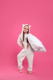 Photo of Cute girl wearing pajamas with pillow on pink background