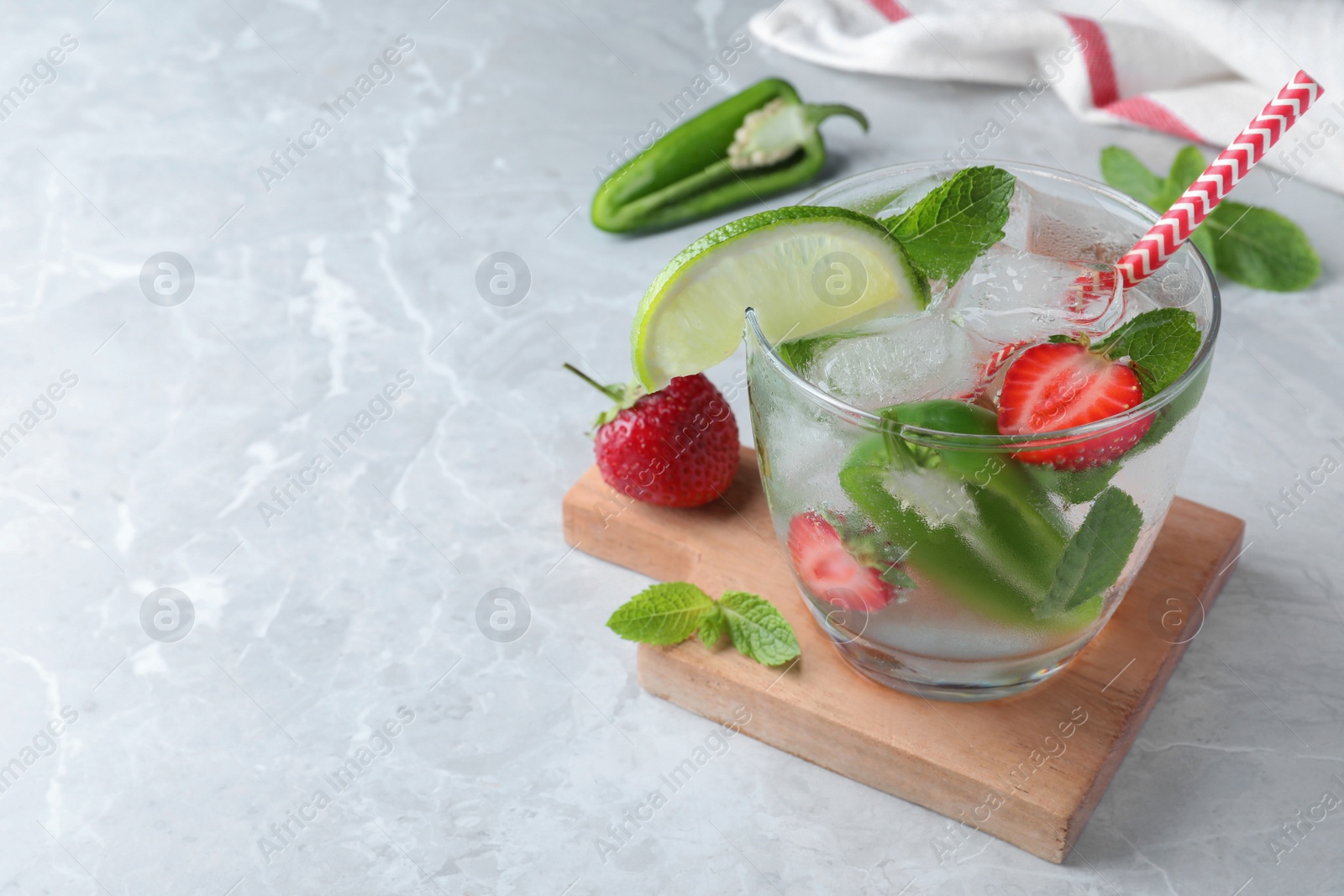 Photo of Spicy cocktail with jalapeno, strawberry, lime and mint on light grey table. Space for text