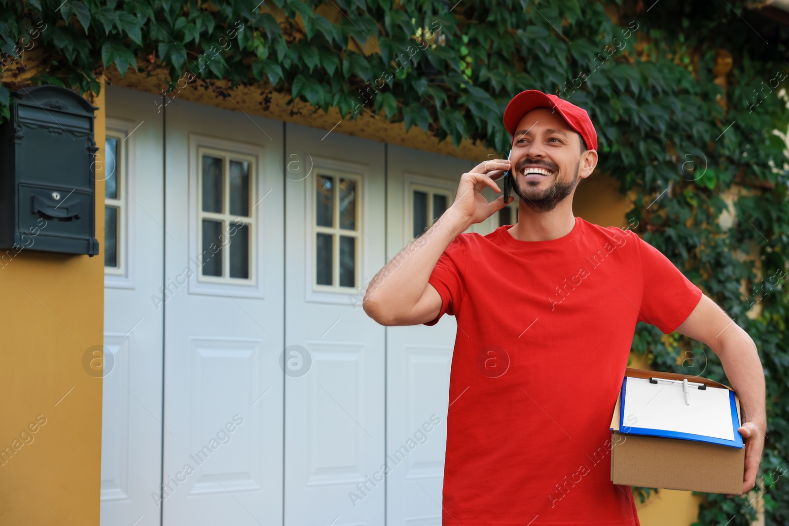 Photo of Courier with parcel talking on smartphone outdoors, space for text. Order delivery