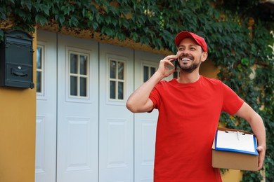 Courier with parcel talking on smartphone outdoors, space for text. Order delivery