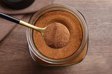 Spoon of instant coffee over jar on wooden table, top view