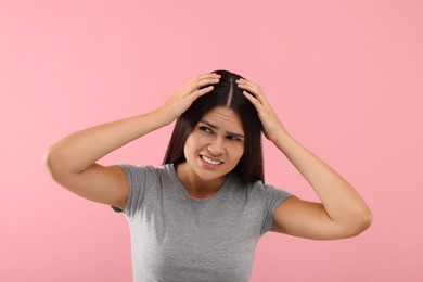 Emotional woman examining her hair and scalp on pink background