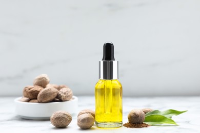 Photo of Bottle of nutmeg oil and nuts on white marble table