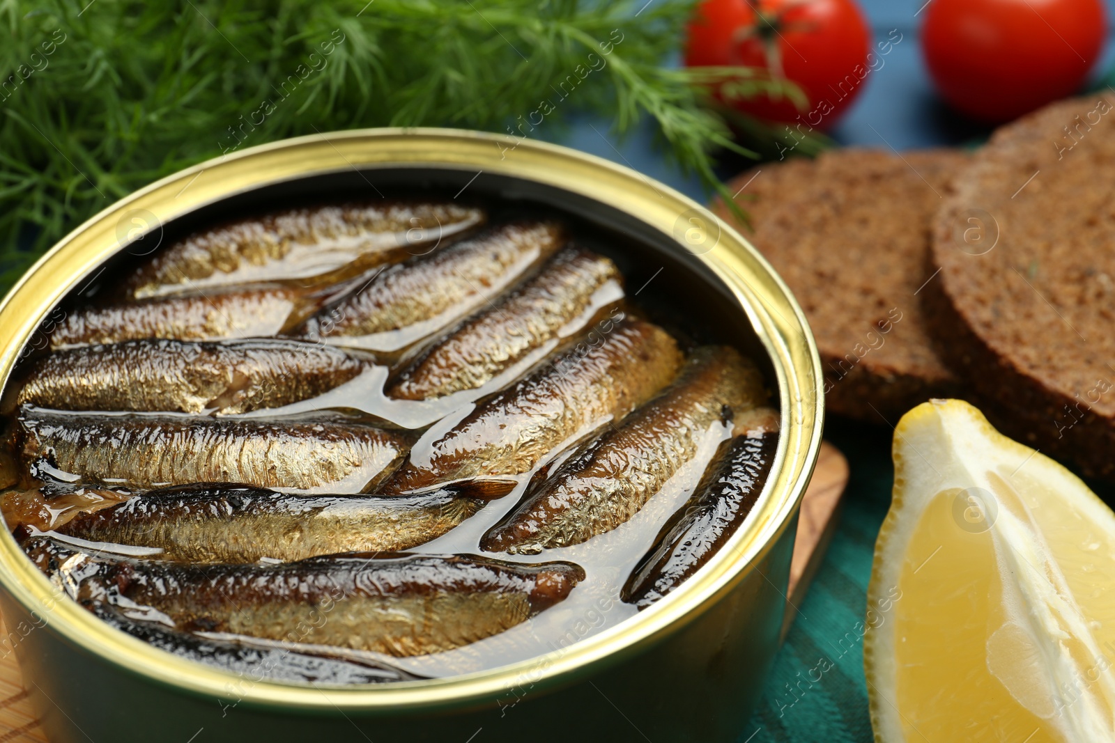 Photo of Tin can with tasty sprats and products on table, closeup