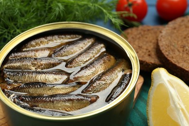 Tin can with tasty sprats and products on table, closeup