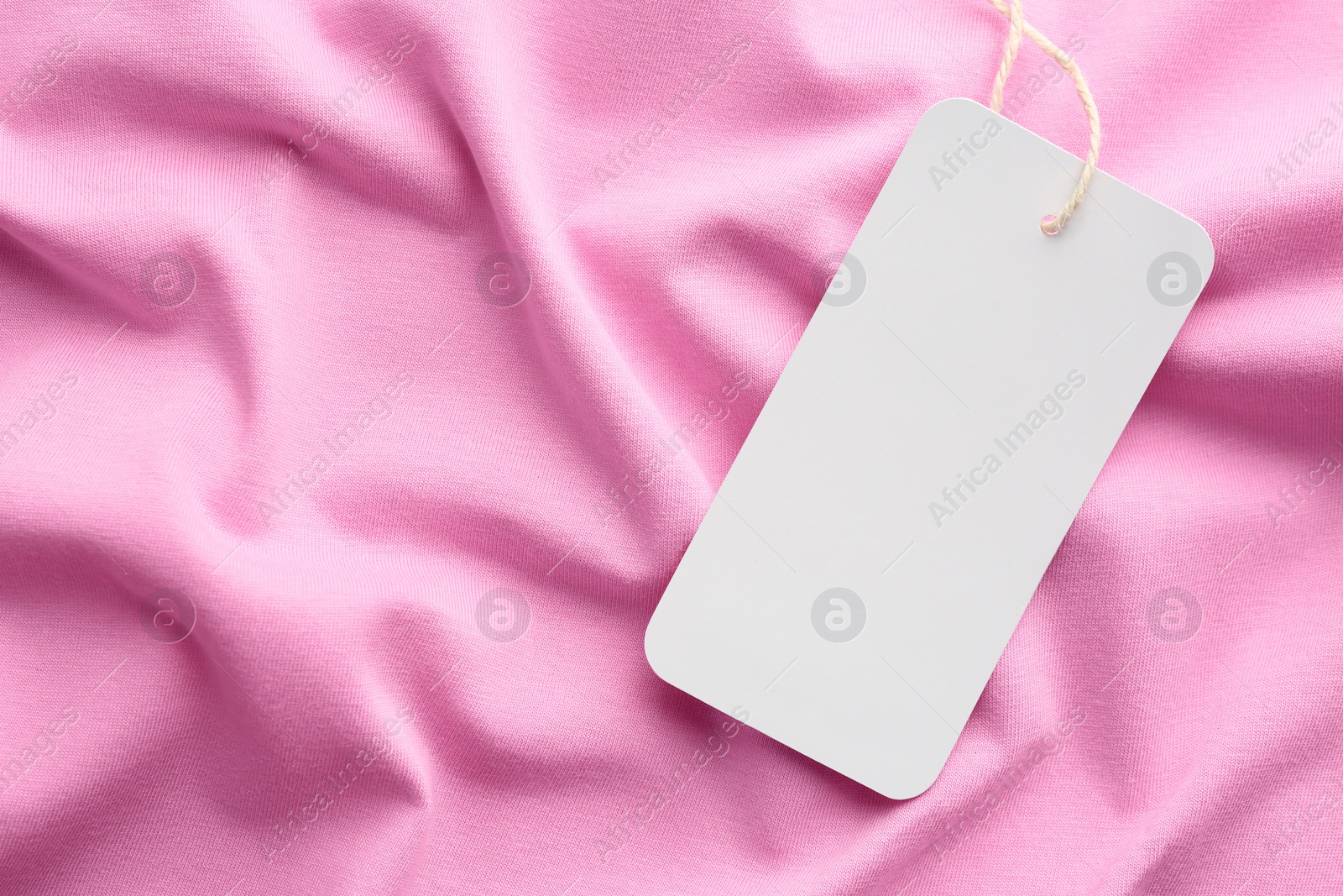 Photo of Cardboard tag with space for text on pink fabric, top view