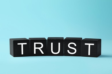 Photo of Word Trust made of black cubes on light blue background