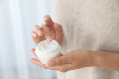 Photo of Young woman holding jar of cream at home, closeup