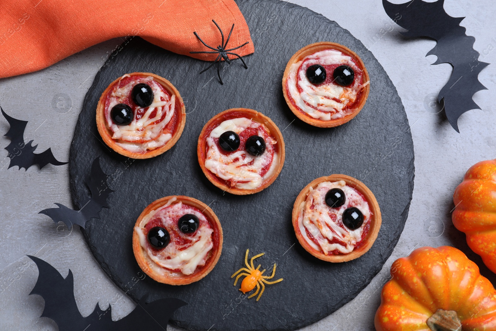 Photo of Cute monster tartlets served on grey table, flat lay. Halloween party food