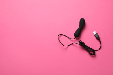 Photo of Black electric powered vibrator on pink background, top view with space for text. Sex toy