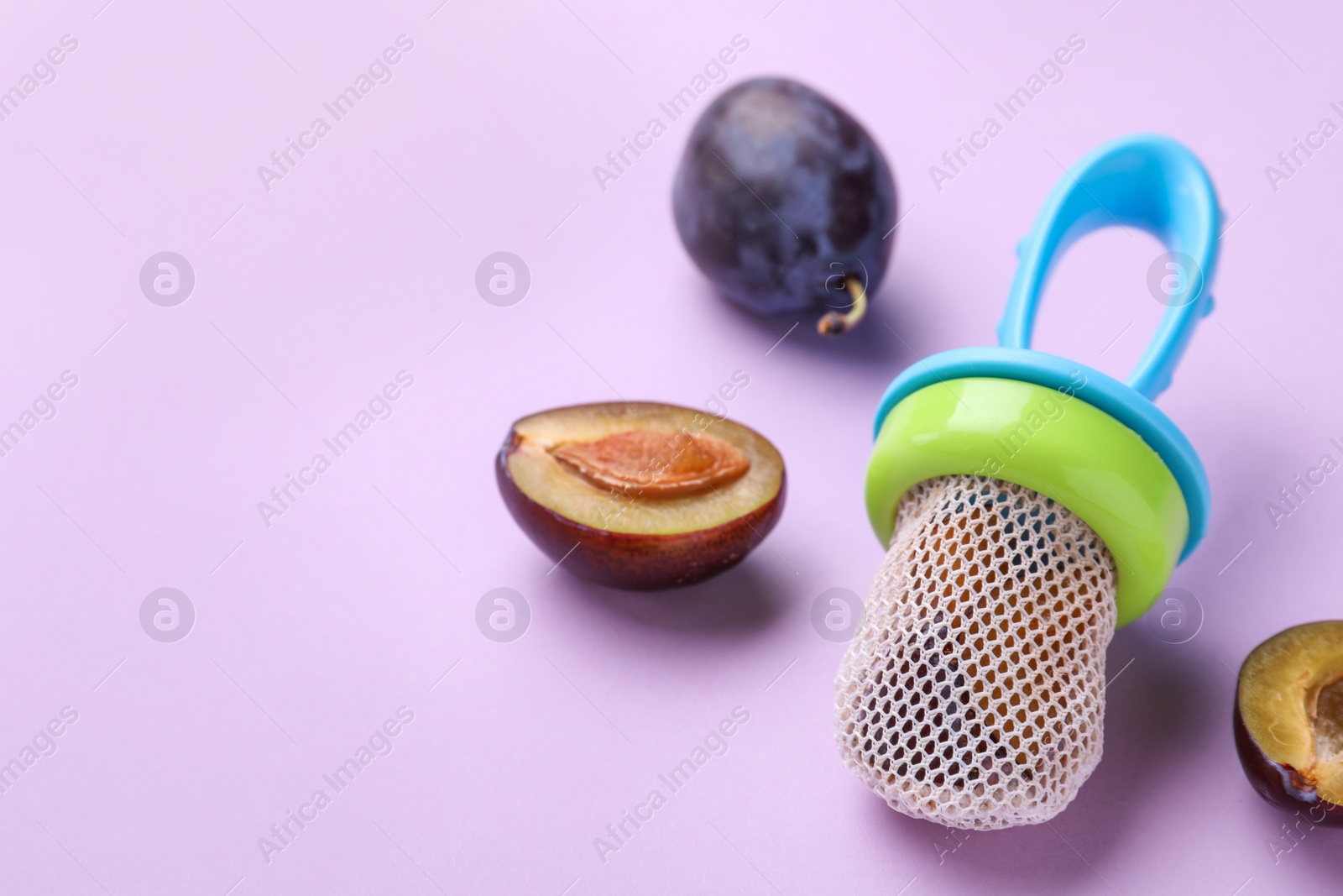 Photo of Nibbler with fresh plum on violet background. Baby feeder