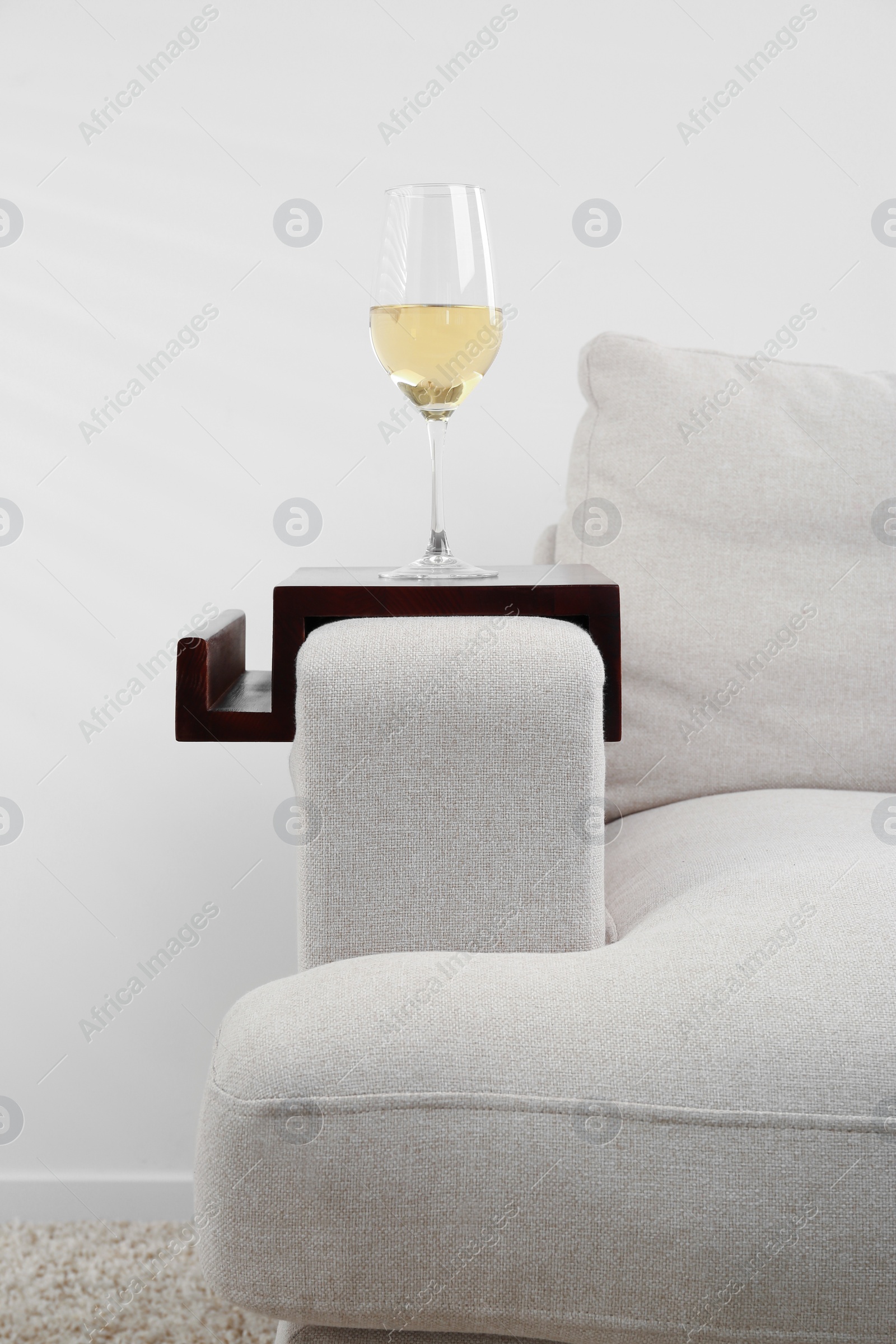 Photo of Glass of white wine on sofa with wooden armrest table indoors. Interior element