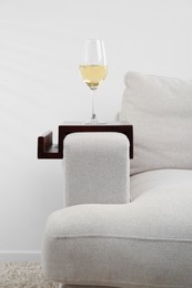 Glass of white wine on sofa with wooden armrest table indoors. Interior element