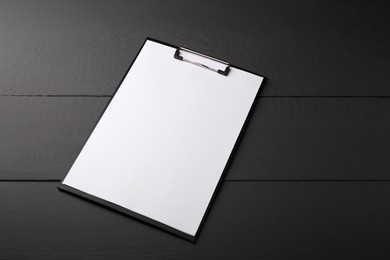 Photo of Clipboard with sheet of paper on black wooden table. Space for text