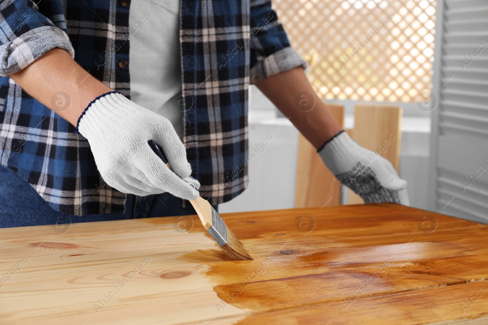 Photo of Man with brush applying wood stain onto wooden surface indoors, closeup