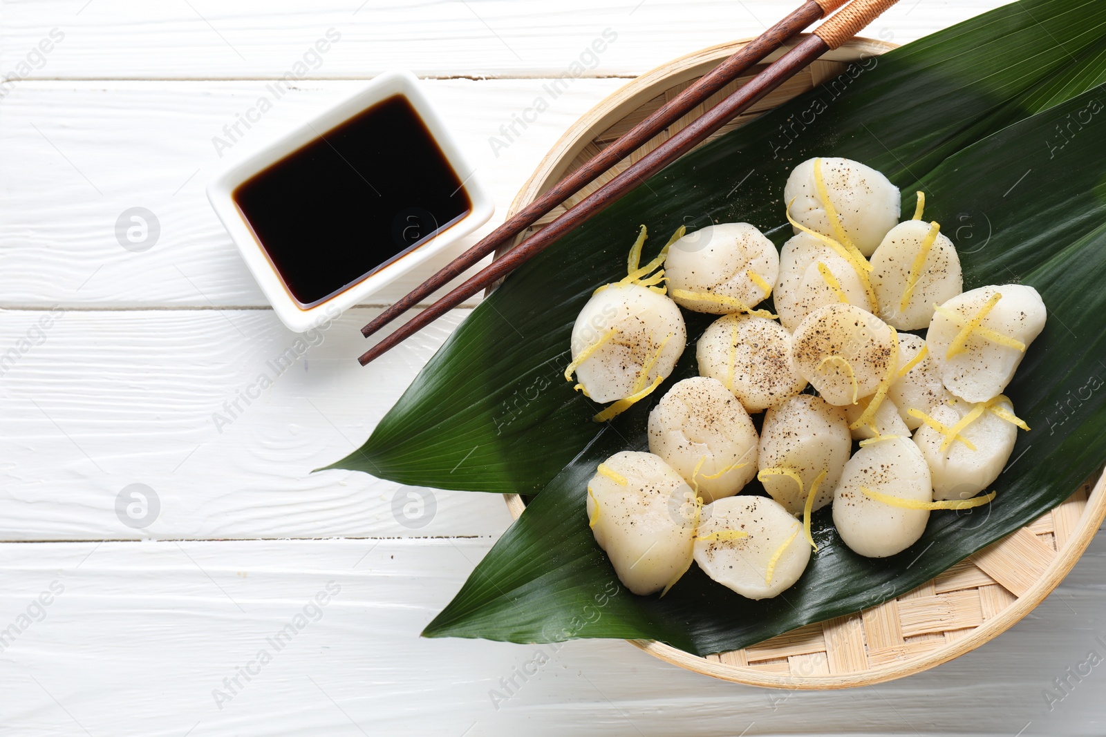 Photo of Raw scallops with milled pepper, lemon zest and soy sauce on white wooden table, flat lay. Space for text