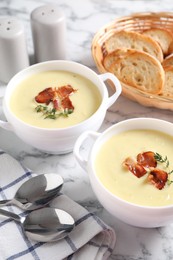 Photo of Tasty potato soup with bacon and rosemary in bowls served on white marble table