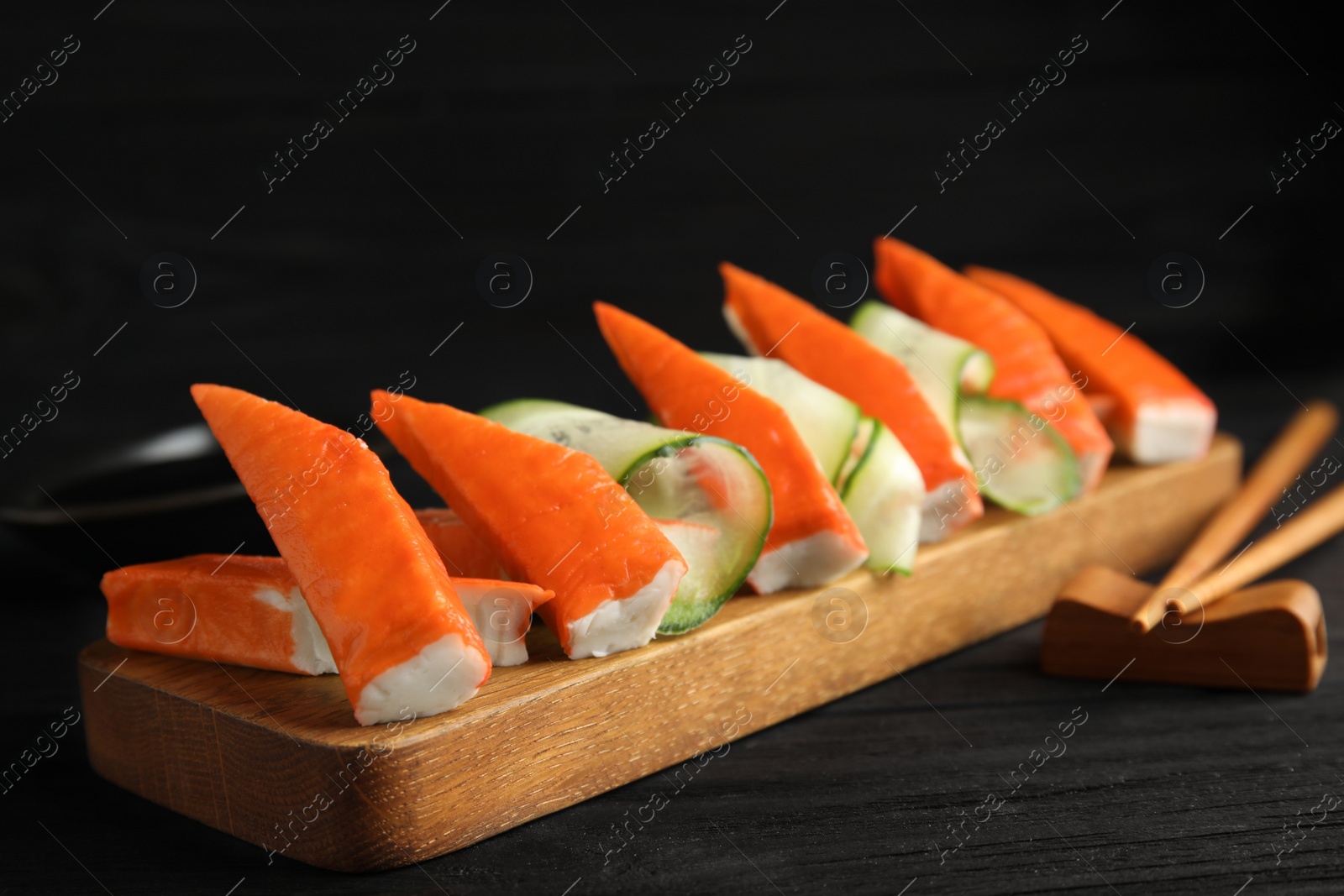 Photo of Wooden board with cut crab sticks and cucumber on table