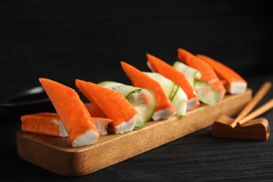 Photo of Wooden board with cut crab sticks and cucumber on table