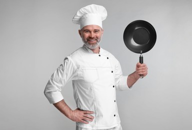 Photo of Happy chef in uniform holding wok on grey background