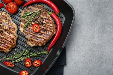 Photo of Grill pan with delicious pork steaks, spices and vegetables on grey table, top view. Space for text