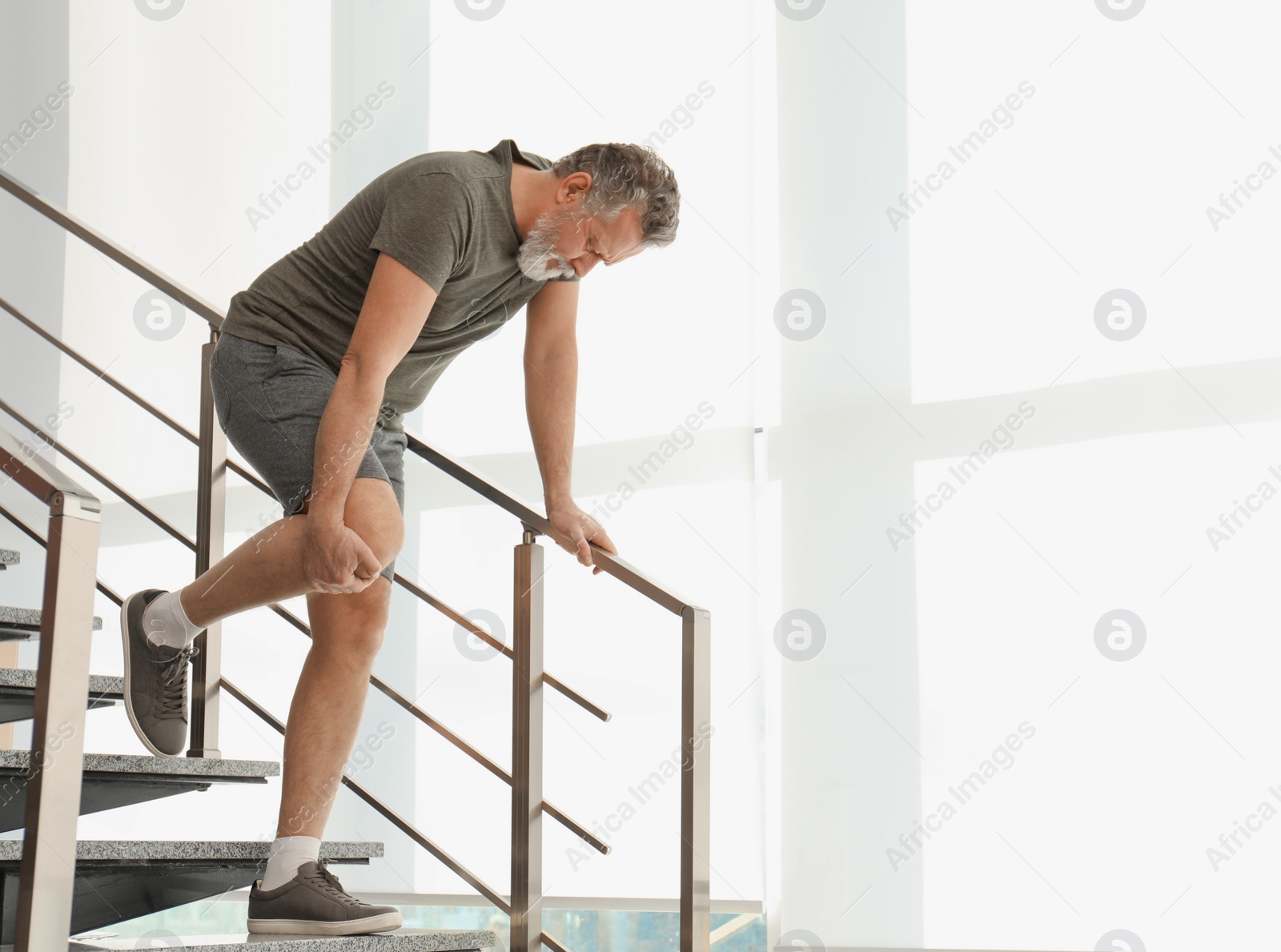 Photo of Senior man suffering from knee pain indoors. Space for text